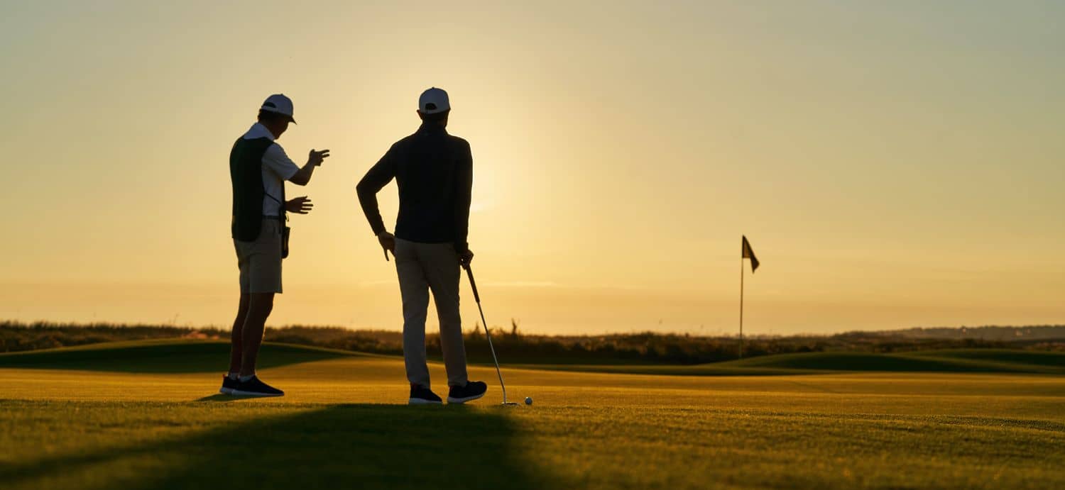 A golfer and caddie reading the green on a course at sunset